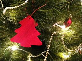 Close-up of a festive Christmas tree adorned with a vibrant red felt tree ornament, sparkling gold beaded garland, and warm string lights. photo