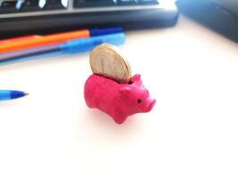 Pink piggy bank on a desk with a coin going in. Represents saving, finance, budget, and investment. Great for financial literacy concepts and articles. photo