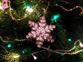 Close-up of a charming snowflake ornament adorned with small bells, hanging on a lush Christmas tree illuminated by warm and cool-toned lights. photo
