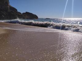 A serene beach on suny day with gentle waves lapping at the shore near a rugged cliff in the distance photo