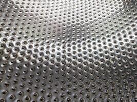 Shiny, dimpled metallic surface with repeating holes. Abstract pattern perfect for backgrounds, textures, or representing industrial concepts like engineering or manufacturing. photo