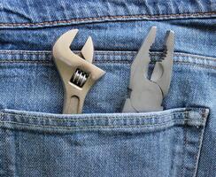 An adjustable spanner and pliers are placed in a jeans pocket. Closeup stock image for home repair theme photo