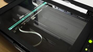 The scanning head of an office scanner moves smoothly beneath the glass surface, illuminating the document as it captures every detail during the scanning process in a modern workspace. video