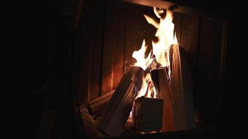 A cozy fireplace with dynamic flames dancing over wooden logs in a dimly lit setting, showcasing flickering motion and glowing embers. video