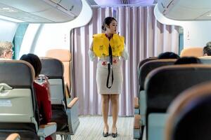 Flight attendant demonstrating emergency life vest usage during in-flight safety briefing for passengers onboard a commercial airplane cabin photo