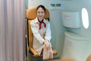 Smiling flight attendant seated on jumpseat with hands folded, ready for takeoff procedures inside passenger aircraft, showing calm and professional demeanor photo