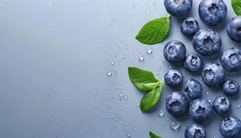 Fresh blueberries with green leaves and water droplets on blue background with copy space top view photo