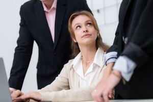 Business meeting featuring a woman and two men discussing work at a desk in a modern office setting during daylight hours photo