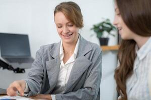 Professional women discussing project details in a modern office setting during the daytime photo