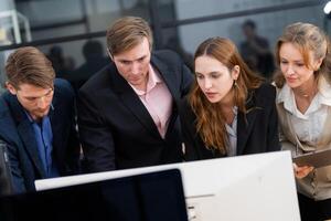 Team collaboration during a business meeting in a modern office setting with individuals focused on a computer screen photo