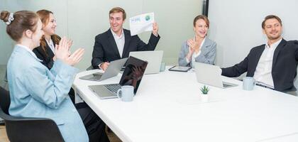Team celebrates successful presentation in modern conference room with laptops and paperwork photo