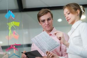Team members collaborate in a modern office discussing project details and reviewing notes on a glass wall covered with sticky notes photo