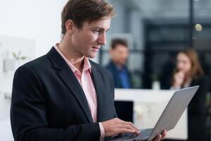 Professional man working on a laptop in a modern office setting with colleagues in the background during a productive meeting photo