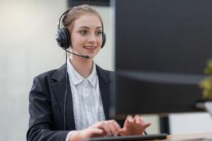 Young woman engaged in remote work while providing customer support at an office desk with a computer and headset photo