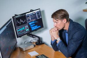 Professional male analyst focused on market data while working at a modern office desk with dual computer monitors photo