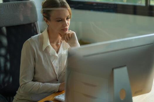 Professional woman deep in thought while working on a computer in a modern office setting during the daytime photo