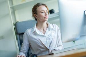 Professional woman working at a desk with a computer in a bright, modern office environment during the daytime photo
