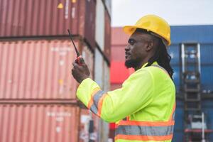 Foreman dock worker in hardhat and safety vest talks on two-way radio control loading containers box from cargo photo