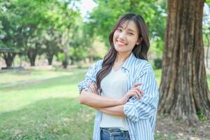 Portrait of a smiling young Asian woman standing in the park with crossed arms and looking at camera photo