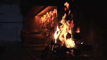 A warm fireplace with vivid flames casting a flickering glow on a stone wall and stacked logs, creating a tranquil and dynamic ambiance. video