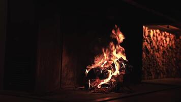 A warmly lit fireplace with dancing flames illuminates a cozy indoor space. Firewood is neatly stacked in the background, creating a relaxing ambiance. video
