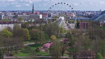 Riga Victory Park in spring with cherry blossoms, the National Library of Latvia, a Ferris wheel, and people strolling among trees and pathways. video