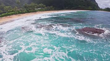 Dynamic aerial view of a Hawaiian beach with turquoise water, rocky formations, lush greenery, and mountains in the background. video