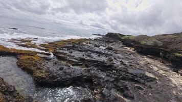 Golden sand beach on Oahu or Kauai, Hawaii, bordered by volcanic rocks and greenery. Two people walk along the shore with waves gently lapping. video