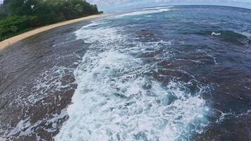 Aerial perspective of a Hawaiian beach bordered by green mountains and forest. Turquoise ocean waves roll gently as a person walks on the shore. video