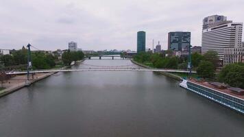 Aerial pan of Frankfurt, Germany, showing the Main River, a pedestrian bridge with people, a historic building, and modern architecture in the background. video