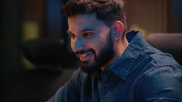 Night computer work smiling Indian Arabian businessman satisfied ethnic guy male business man ceo programmer manager entrepreneur online typing laptop computer commerce project in dark evening office video