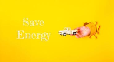 Hand holding a toy truck with the words Save Energy written below it photo