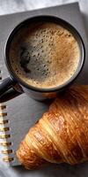 A cup of coffee and croissant on a notebook photo