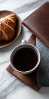 A coffee cup, croissant and notebook on a marble counter photo