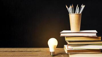 Light bulb is lit up on a table with a stack of books and pencils photo