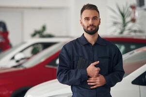 In blue ,,colored ,uniform. Car repairman is in the garage with automobile photo