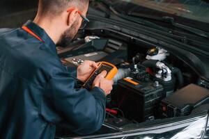In blue, colored ,,uniform. Car repairman is in the garage with automobile photo