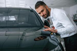 Looking at polished surface. Worker in formal clothes is in the auto salon photo