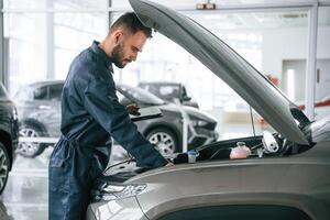 View from the side., Car repairman, is in the garage with automobile photo