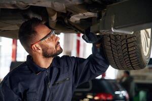 In protective, eyewear, under vehicle. Car repairman is in the garage with automobile photo