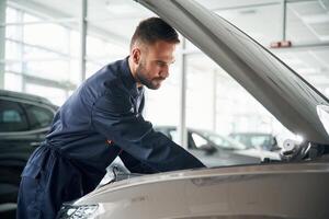 Hood of vehicle is,, opened. Car repairman is in the garage with automobile photo