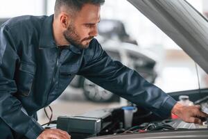 With device, for measuring electricity. Car repairman is in the garage with automobile photo
