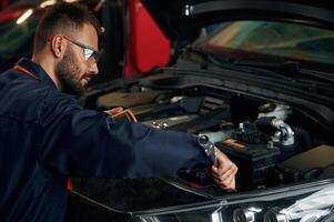 In ,blue ,colored uniform. Car repairman is in the garage with automobile photo