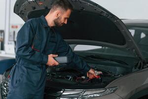With device for measuring, electricity.. Car repairman is in the garage with automobile photo