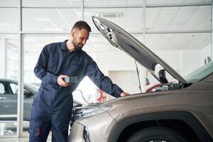 Device for measuring voltage ,is in hands. Car repairman is in the garage with automobile photo