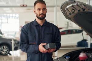 With device for ,measuring electricity. Car repairman is in the garage with automobile photo