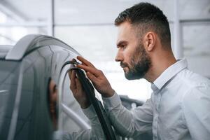 Looking, ,at polished surface. Worker in formal clothes is in the auto salon photo