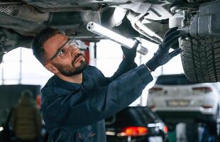 Under ,the, vehicle, fixing. Car repairman is in the garage with automobile photo