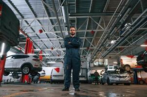 Standing, and, posing. Car repairman is in the garage with automobile photo