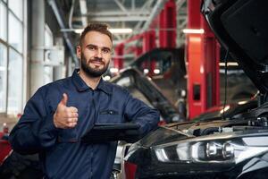 Using ,tablet.. Car repairman is in the garage with automobile photo